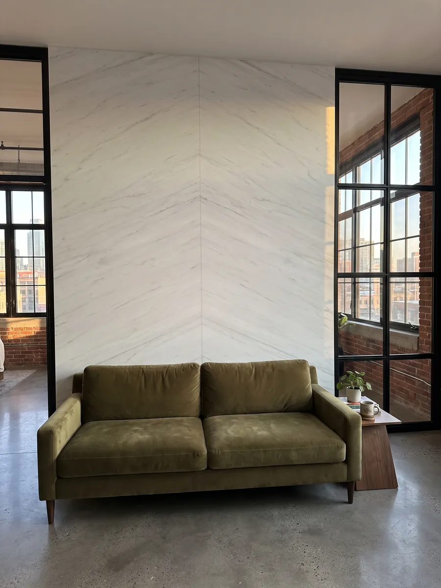 Living room wall clad in bookmatched Snow White marble slabs behind a sofa: a very clean white with barely visible gray traces running diagonally