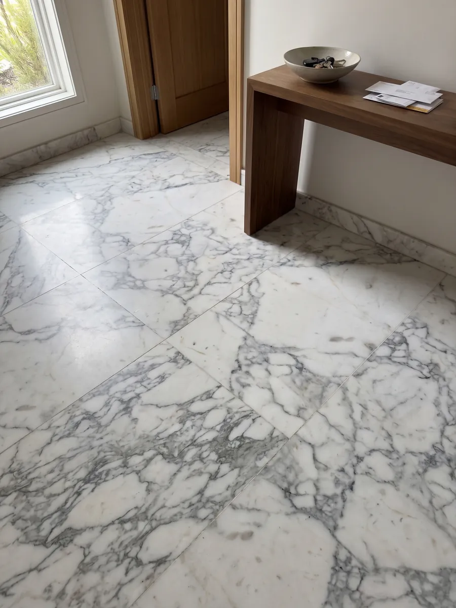 Entryway floor in large Bianco Statuarietto marble slabs with natural light: a white with a net of gray veins around fragments, concentrated in the lower part