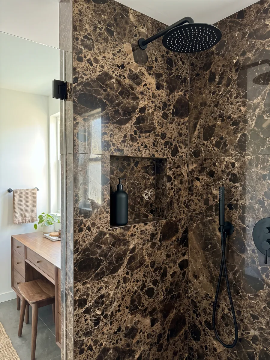 Shower clad in full Emperador Dark marble slabs with a recessed niche: almost black dark brown patches joined by a dense beige web