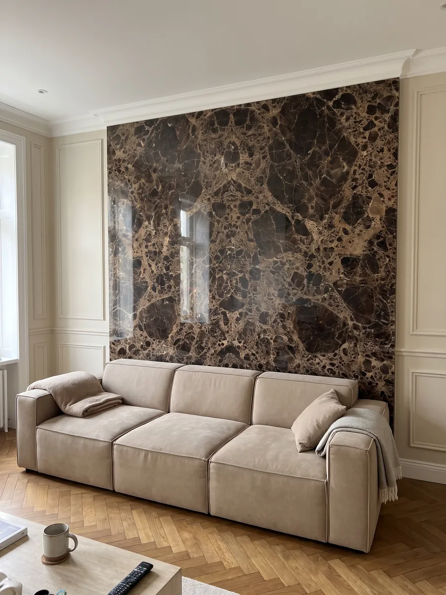 Living room wall clad in bookmatched Emperador Dark marble slabs behind a sofa: almost black dark brown patches joined by a dense beige web
