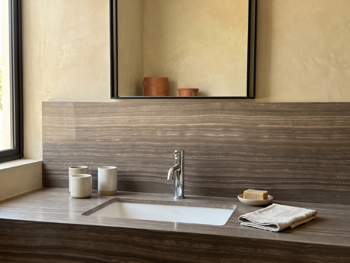 Bathroom vanity top and wall in Eramosa marble with a white sink and chrome faucet: grayish brown with fine, parallel horizontal wood-like lines