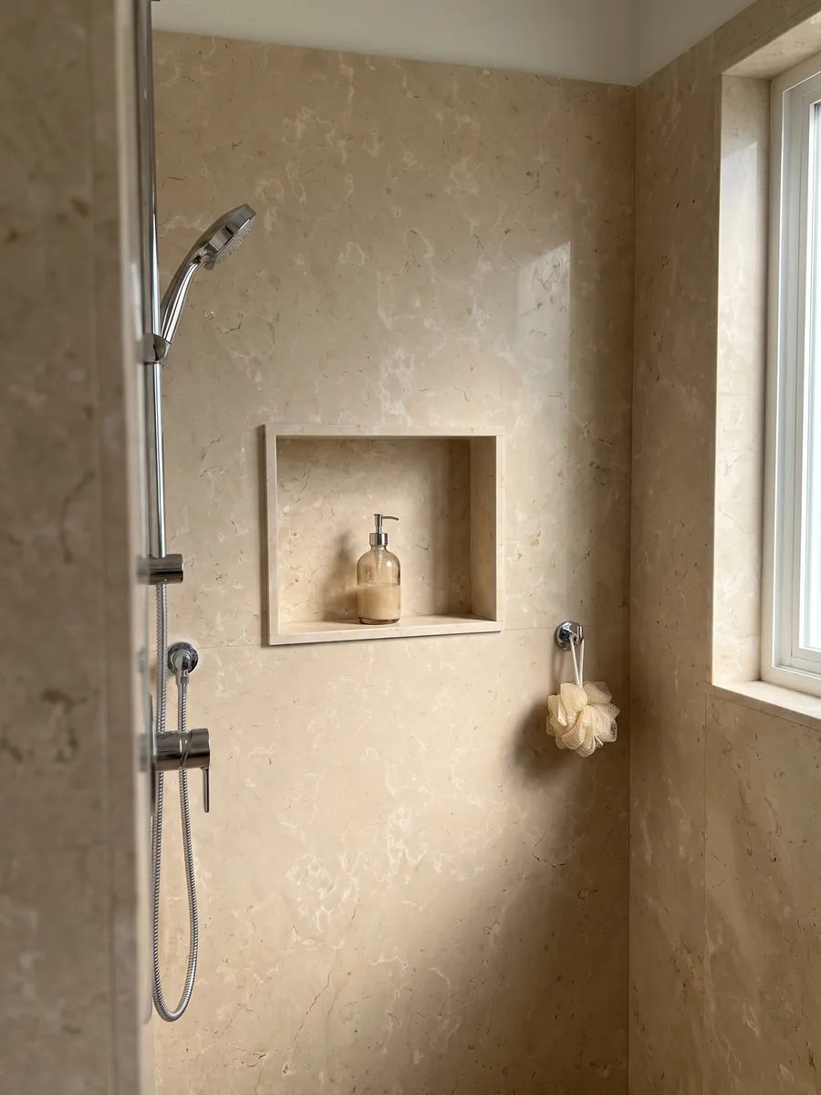 Shower clad in full Crema Nuova marble slabs with a recessed niche: warm cream with soft, diffused light patches
