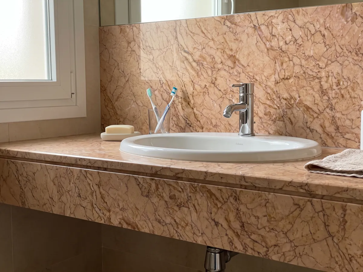 Bathroom vanity top and wall in Crema Valencia marble with a white sink and chrome fixtures: pinkish salmon with a dense web of fine brown veins