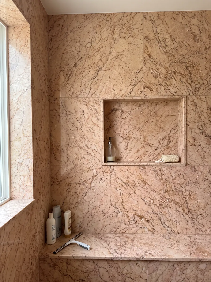 Shower clad in full Crema Valencia marble slabs with a recessed niche: pinkish salmon with a dense web of fine brown veins