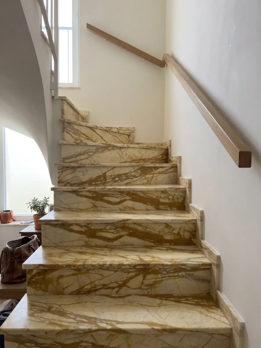 Interior staircase with golden Calacatta Siena marble steps and a handrail: pale yellow with a web of thick golden ochre veins running horizontally