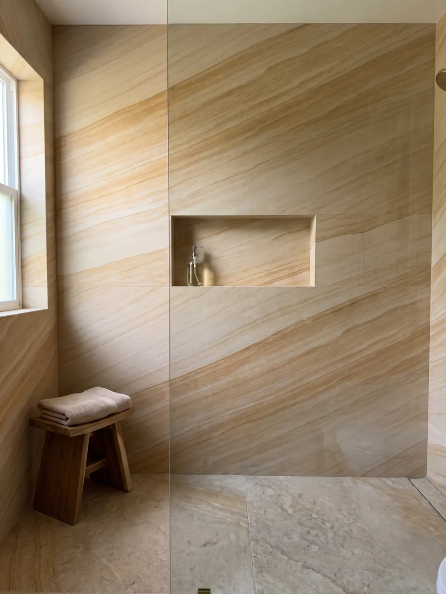 Shower clad in full slabs of golden Douglas marble with a recessed niche: parallel ocher and cream bands running diagonally, with a sandstone look