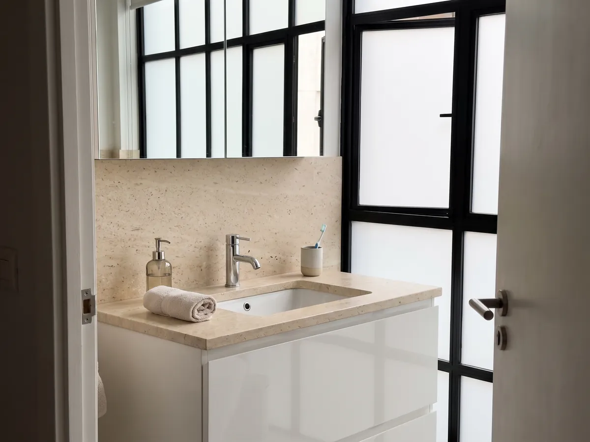 Bathroom vanity top and wall in Fior di Crema marble with a white sink and chrome faucets: a very even cream surface, fine grained, with no visible veins