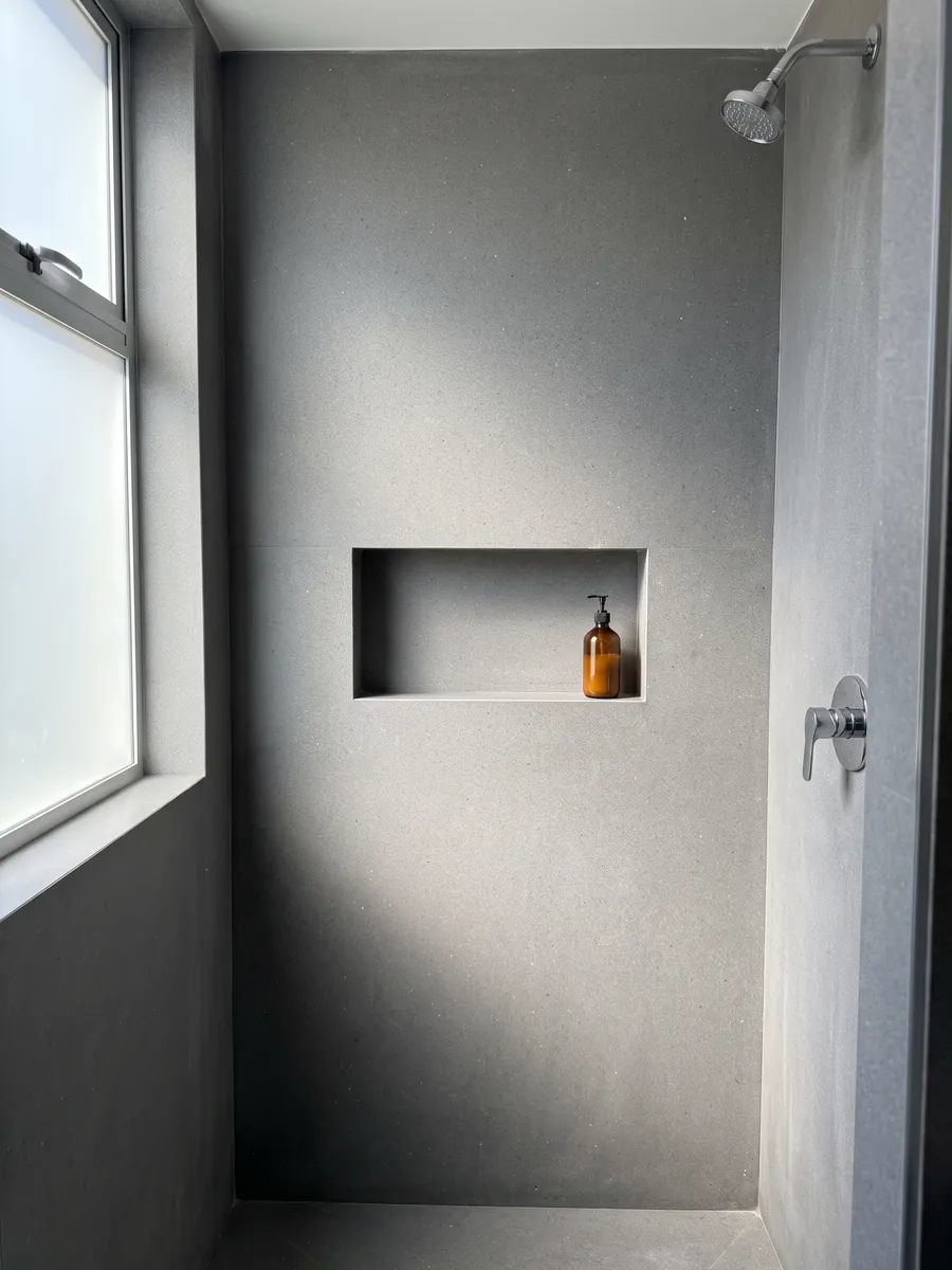 Shower clad in full slabs of Grigio Aitos marble with a recessed niche: medium gray, fine grained, evenly speckled, no veins