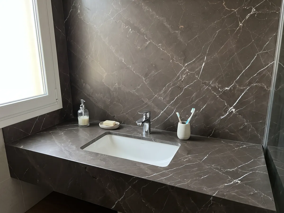 Vanity top and bathroom wall in Grigio Amani marble with a white sink and chrome faucets: dark taupe background crossed by fine white diagonal veins