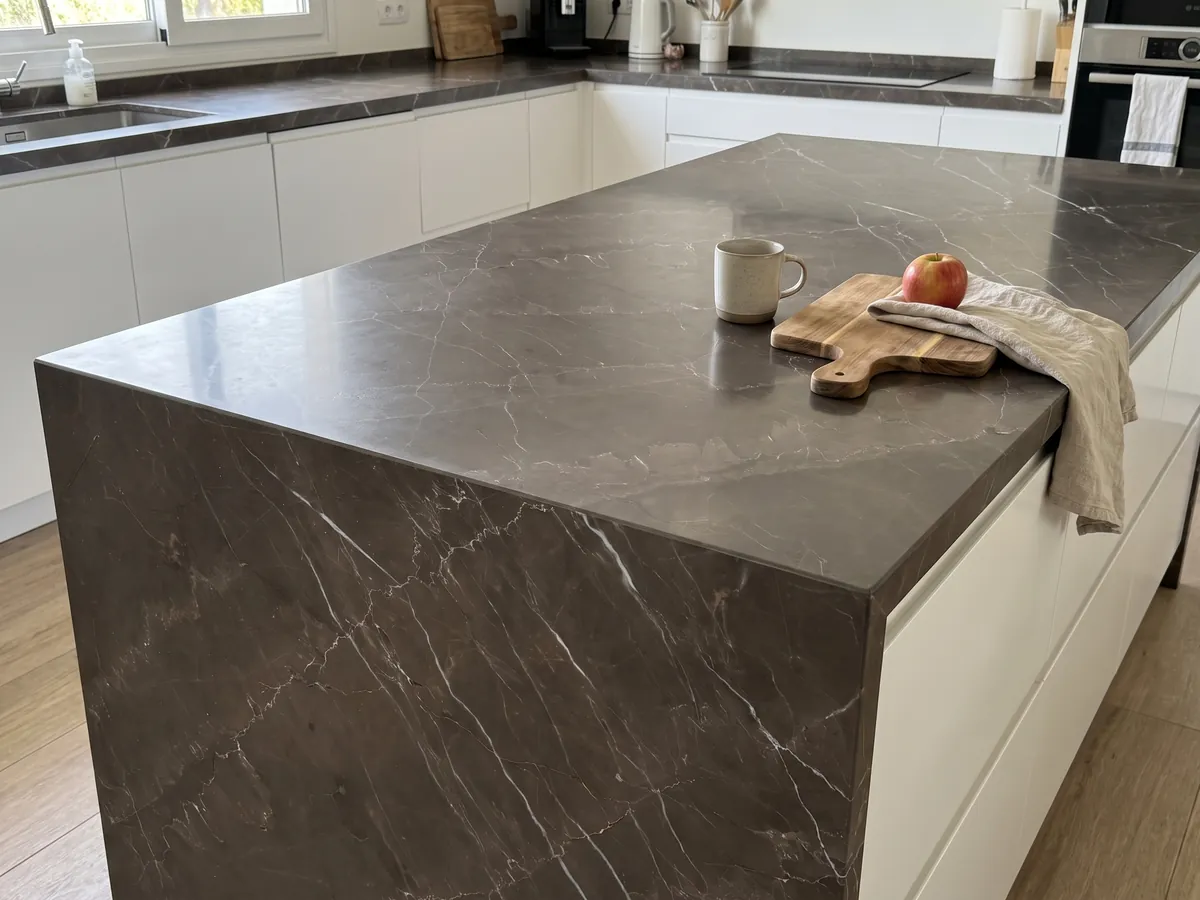 Kitchen island with a brown Grigio Amani marble countertop and straight edge in a kitchen with natural light: a dark taupe base crossed by fine white diagonal veins