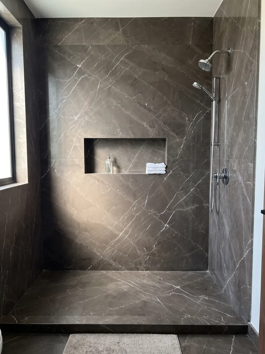 Shower clad in full Grigio Amani marble slabs with a recessed niche: dark taupe background crossed by fine white diagonal veins