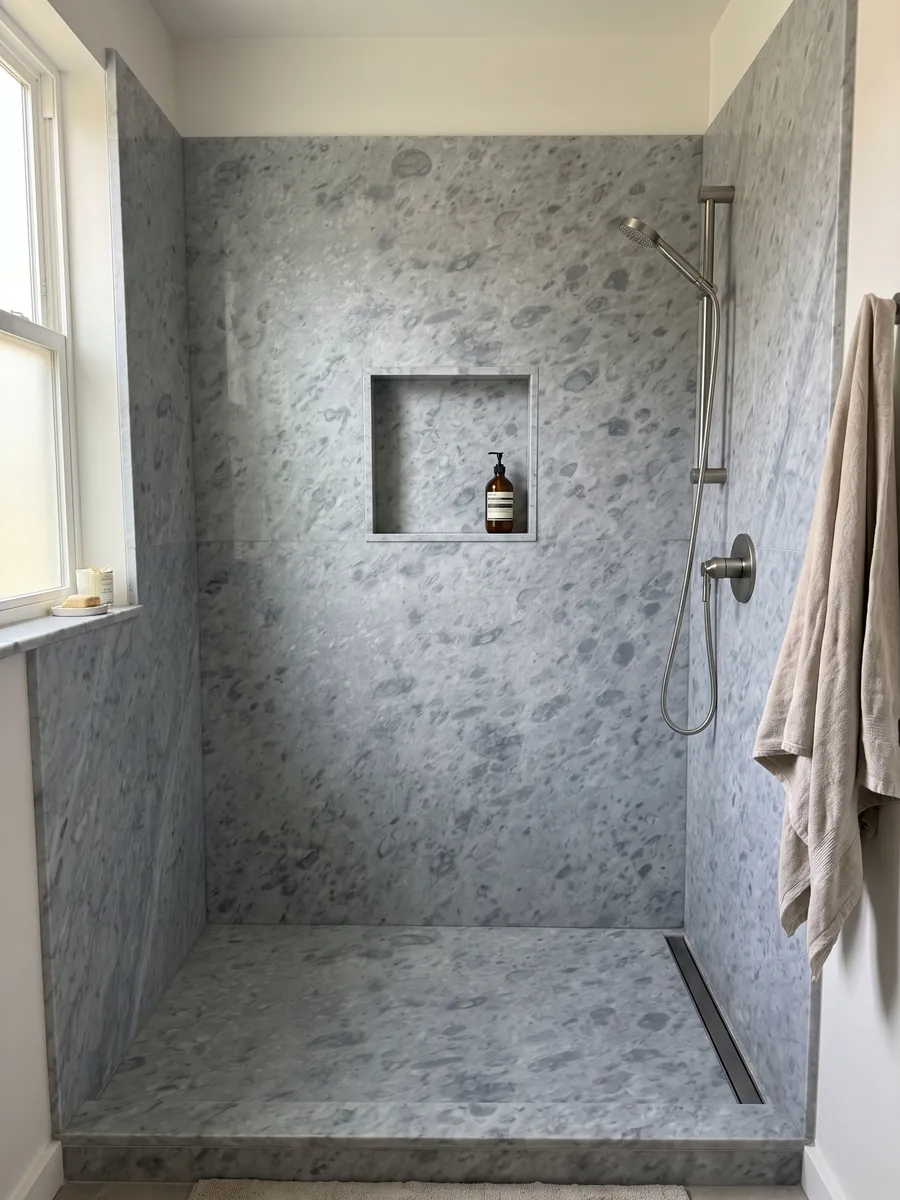 Shower clad in full gray Bardiglio Imperiale marble slabs with a recessed niche: even blue-gray with round spots slightly darker