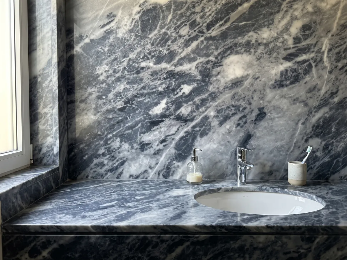 Vanity top and bathroom wall in gray Bardiglio Nuvolato marble with a white sink and chrome fixtures: dark blue-gray with diffuse whitish clouds and veins in diagonal