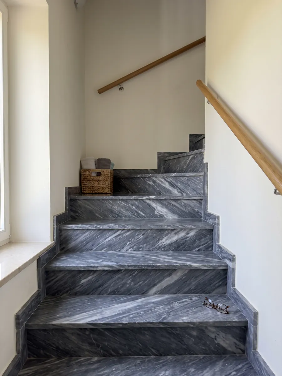 Indoor staircase with gray Bardiglio Nuvolato marble treads and a handrail: dark blue-gray with diffuse whitish clouds and veins in diagonal