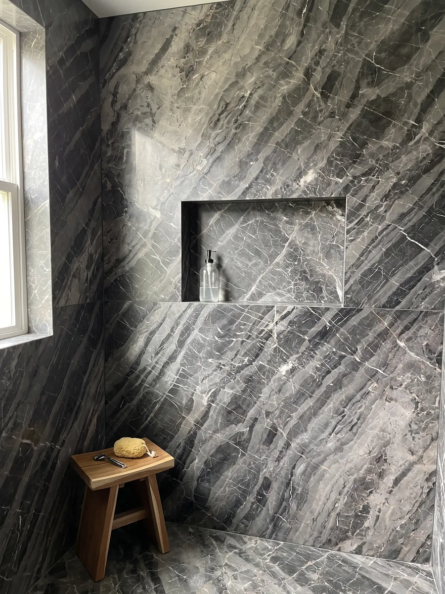 Shower clad in full gray Bellagio marble slabs with a recessed niche: gray bands stepped on the diagonal with a fine network of white veins