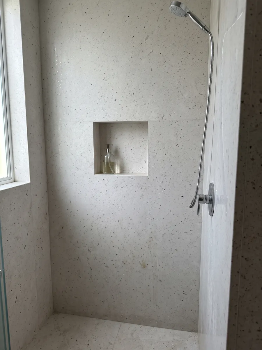 Shower clad in full slabs of gray Bianco Martel marble with a recessed niche: smooth light gray with many small dark dots spread across it