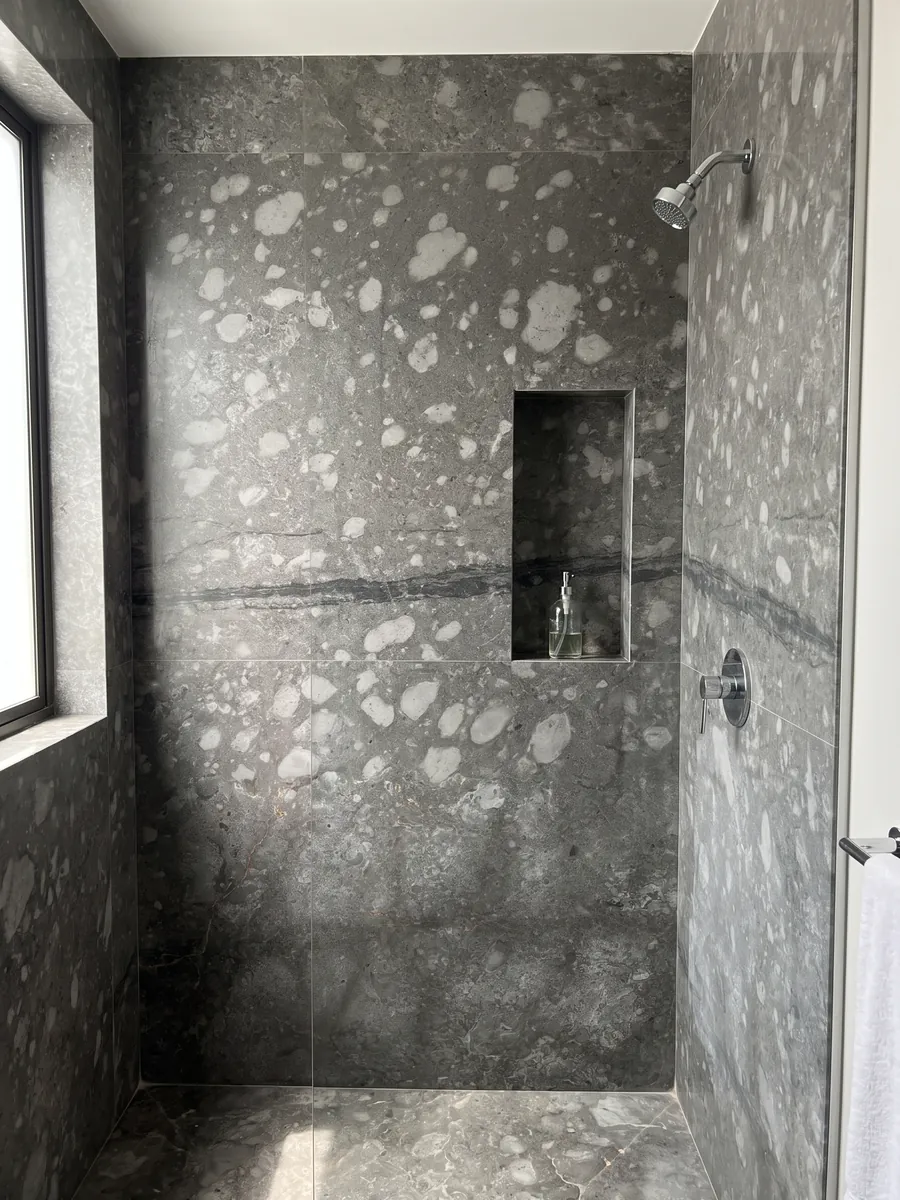 Shower clad in full Grigio Billiemi marble slabs with a recessed niche: gray with light cloud-shaped patches and a dark horizontal band