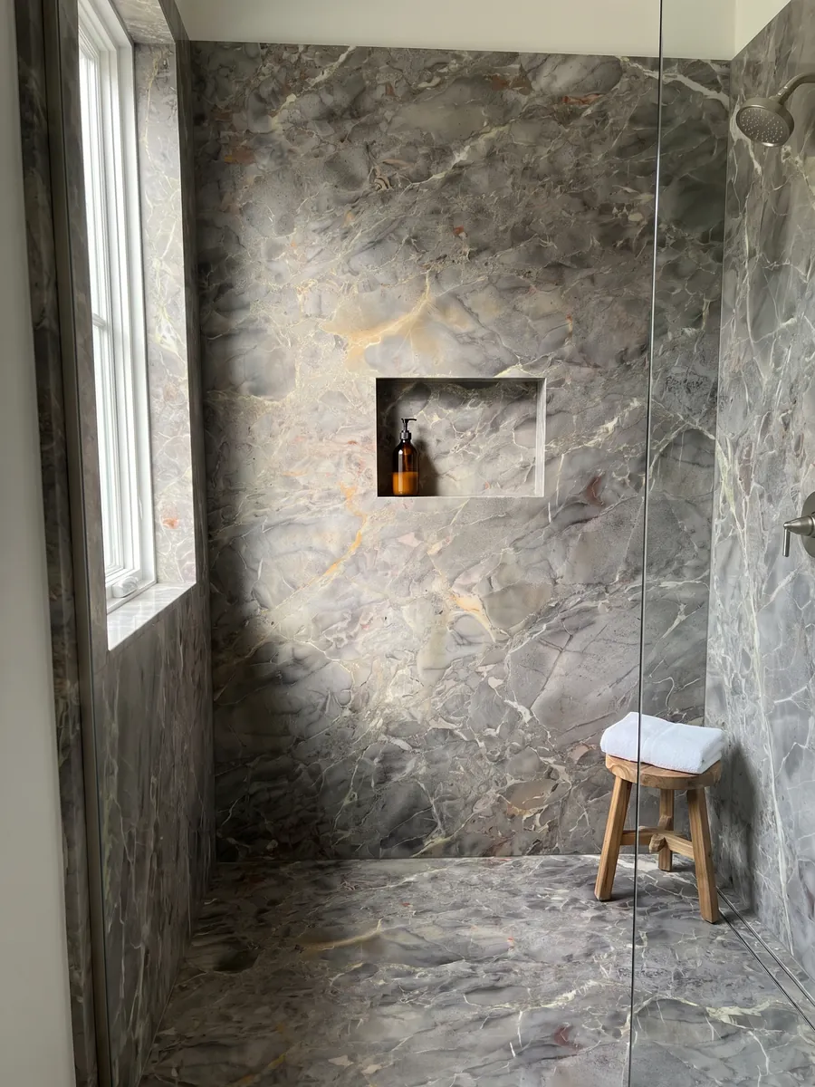 Shower clad in full slabs of gray Breccia di Versailles marble with a recessed niche: gray-brown with soft-edged fragments, fine light veins and ochre touches