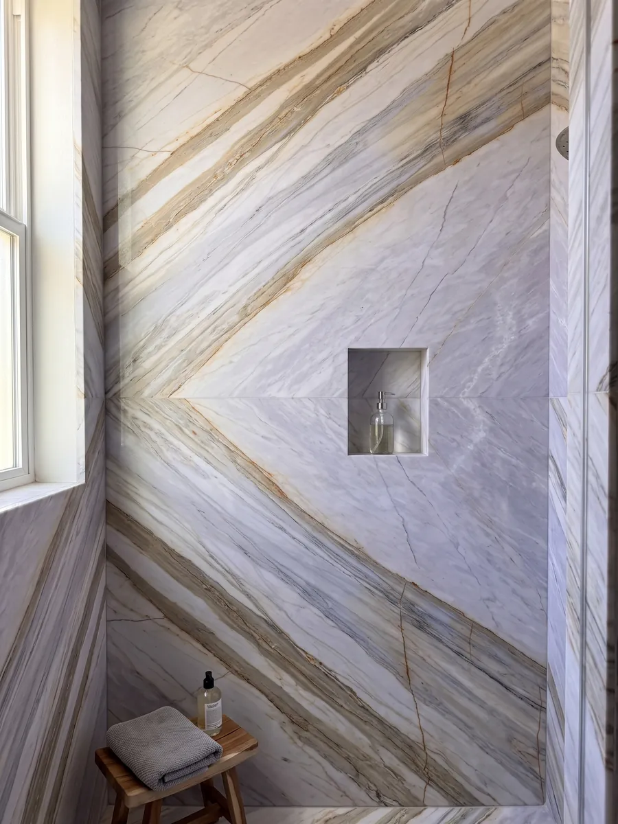 Shower clad in full slabs of gray Calacatta Supreme marble with a recessed niche: light lavender gray with diagonal beige bands and fine ocher lines