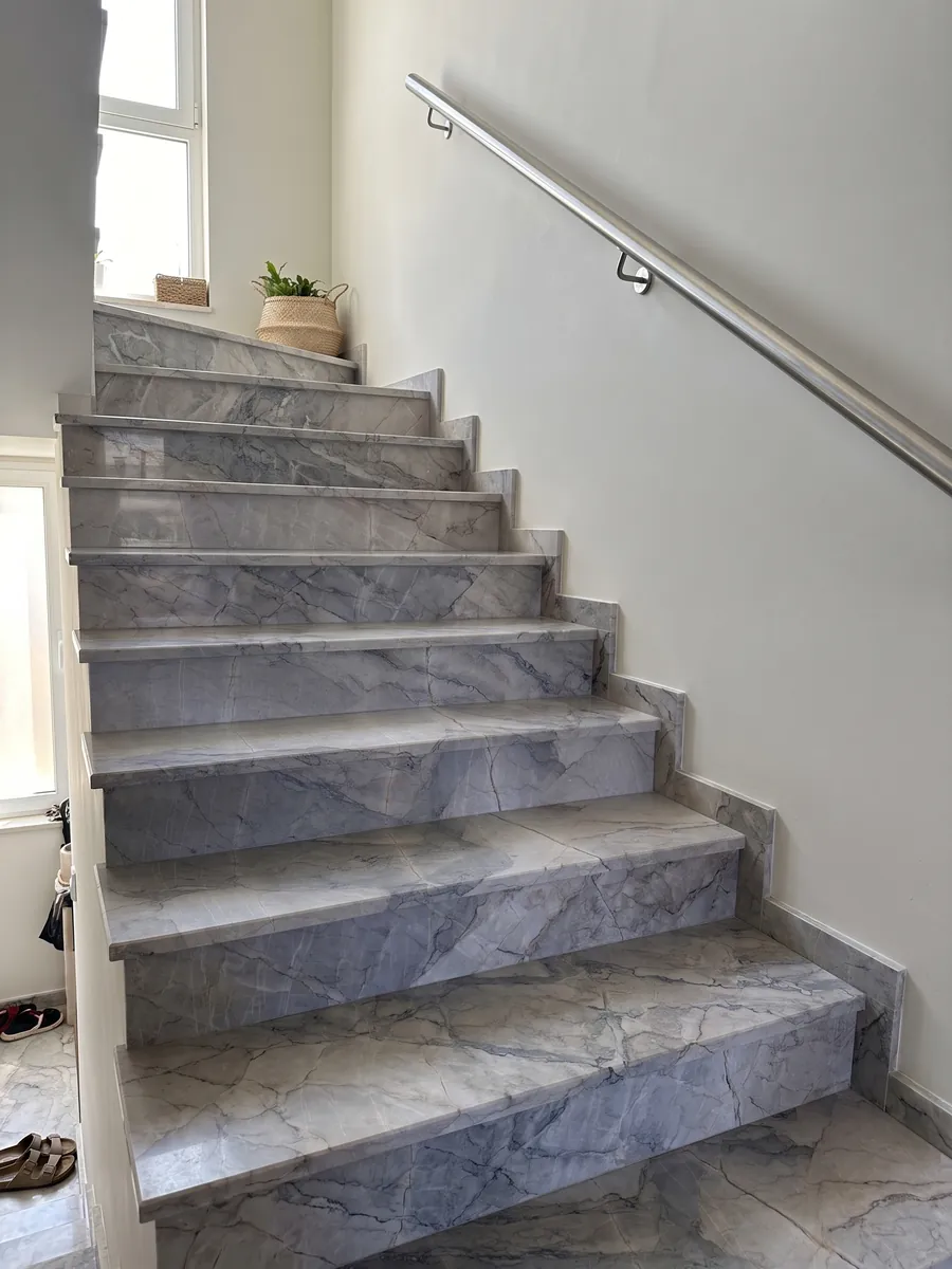 Interior staircase with gray Camouflage marble treads and a handrail: lavender-gray and blue-gray fragments with fine veins in a mosaic pattern