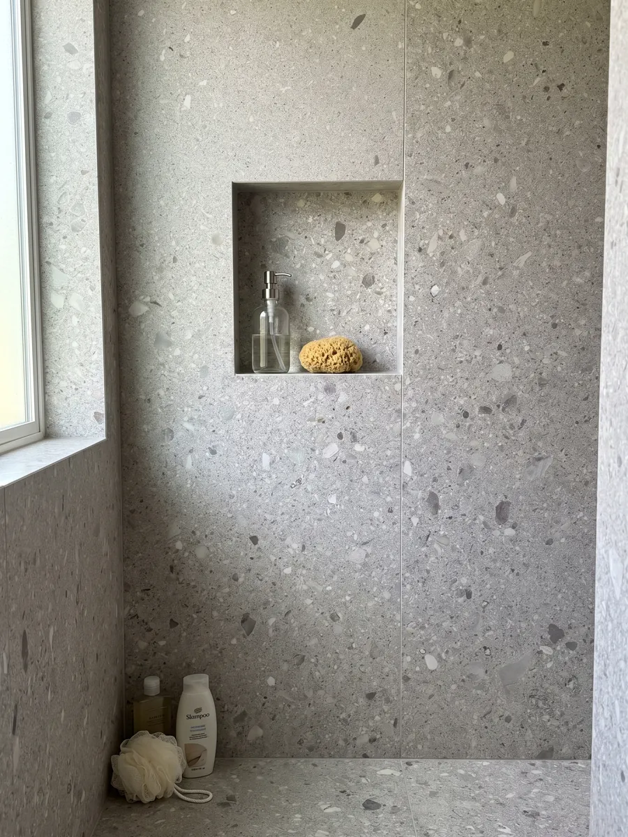 Shower clad in full slabs of gray Ceppo di Gré marble with a recessed niche: light gray with small beige and gray fragments spread across it