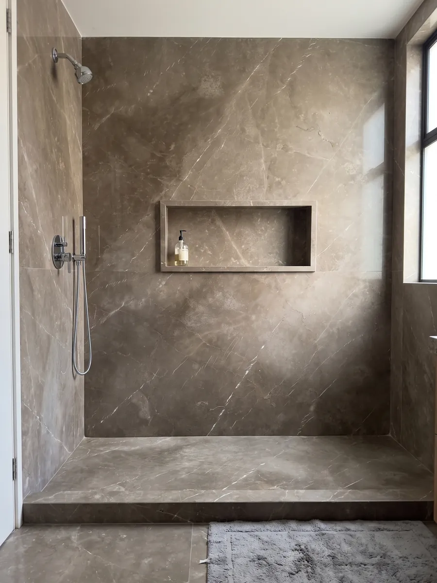 Shower clad in full Grigio Collemandina marble slabs with a recessed niche: cloudy brown-gray with few, very fine white veins