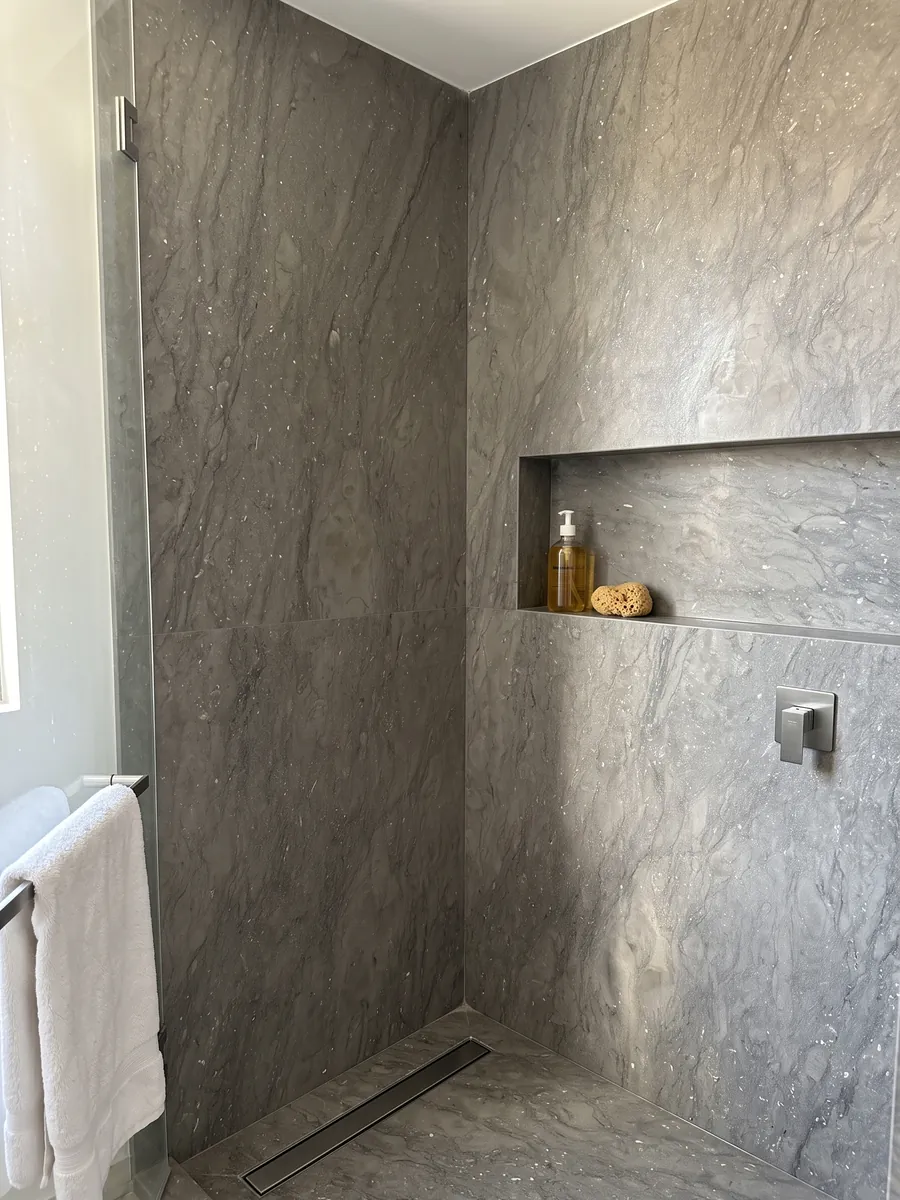 Shower clad in full slabs of gray Ebano marble with a recessed niche: an even gray-brown with small sparkling light specks