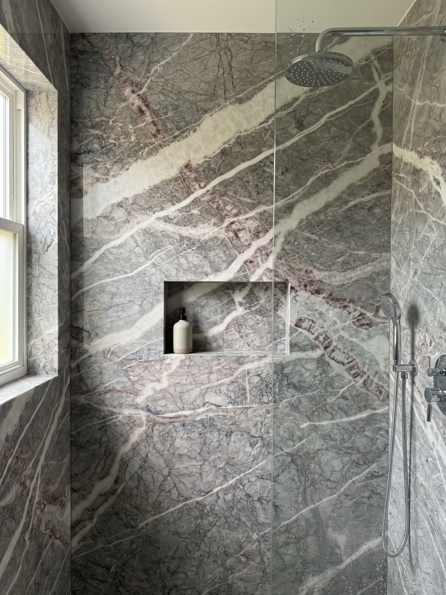 Shower clad in full gray Fior di Pesco Carnico marble slabs with a recessed niche: diagonal white veins joined by wine-colored veins over a gray with a network of fine lines