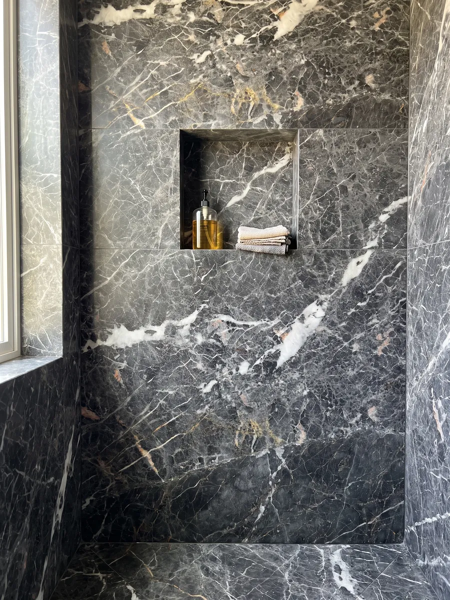 Shower clad in full slabs of Grey Saint Laurent gray marble with a recessed niche: dark gray with elongated white patches and a fine network of light and golden veins