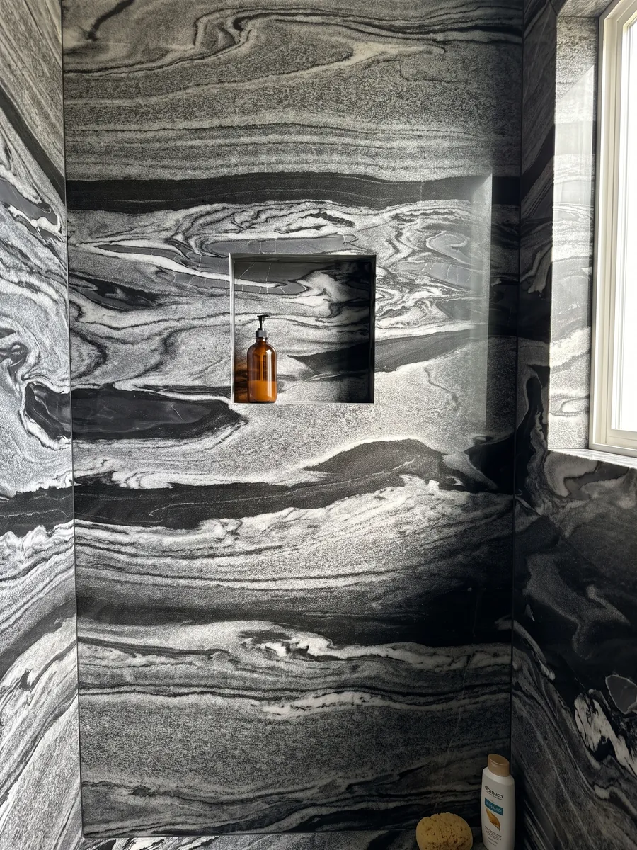Shower clad in full Grigio Imperiale marble slabs with a recessed niche: horizontal gray and white waves over black, like moving currents