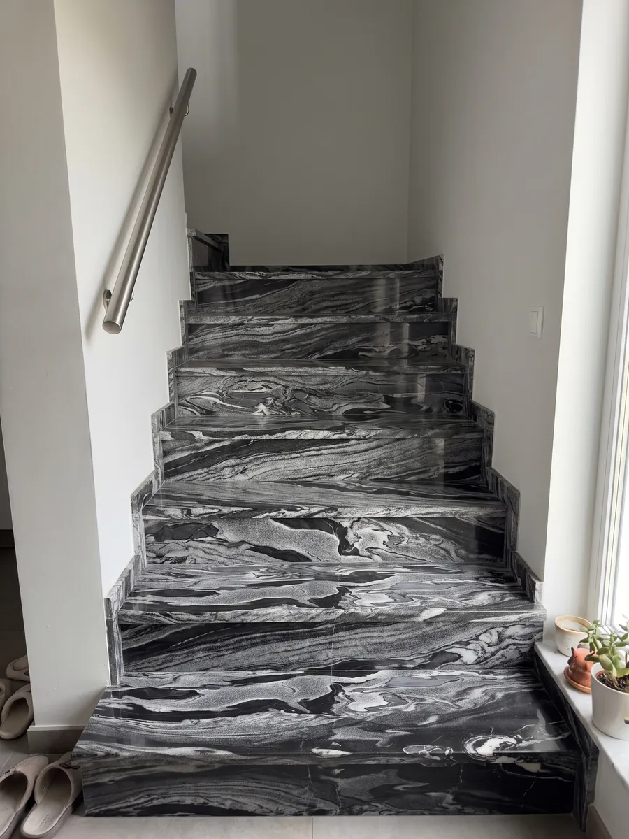 Interior staircase with Grigio Imperiale marble treads and a handrail: horizontal gray and white waves over black, like moving currents