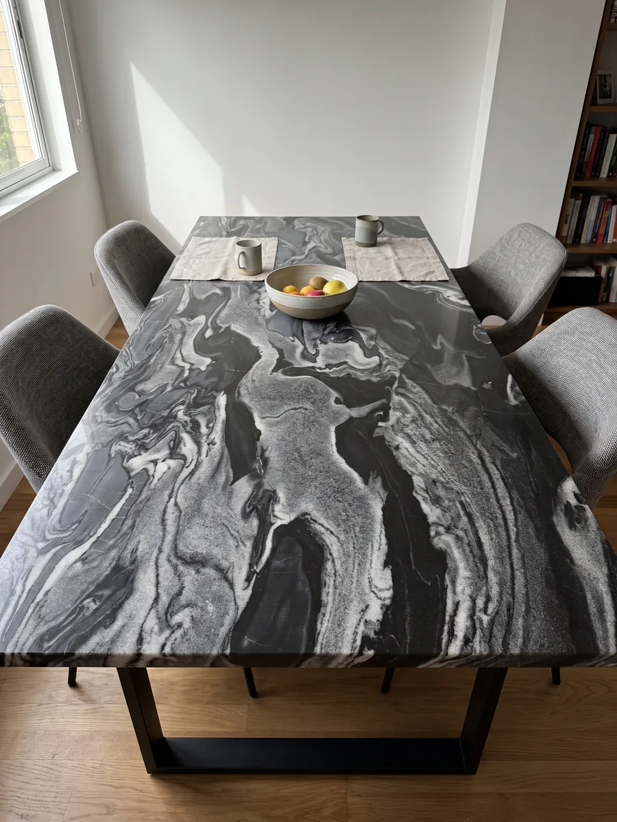 Dining table with a Grigio Imperiale marble top on a steel base: horizontal gray and white waves over black, like moving currents
