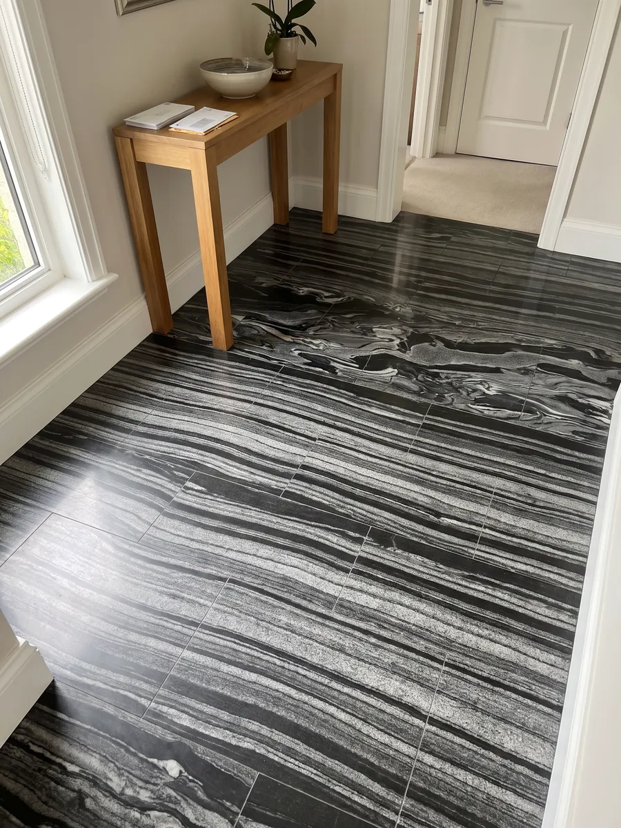 Entryway floor in large Grigio Imperiale marble slabs with natural light: horizontal gray and white waves over black, like moving currents