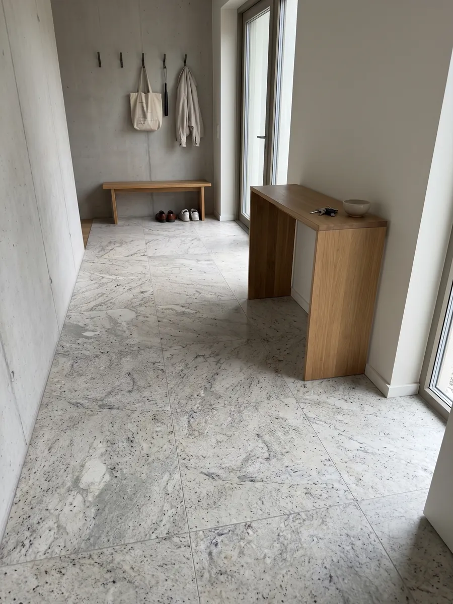Entryway floor in large slabs of gray Lemon Ice marble with natural light: light gray speckled with dark flecks, resembling granite