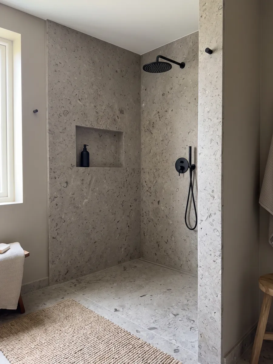 Shower clad in full slabs of gray Lipica Fiorito marble with a recessed niche: beige gray with small dark fossil figures spread across the slab