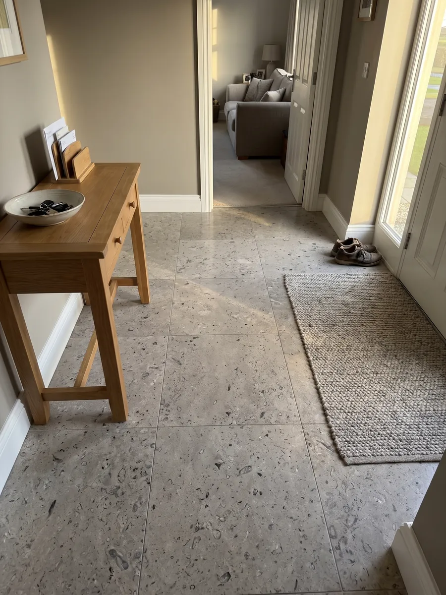 Entryway floor in large slabs of gray Lipica Fiorito marble with natural light: beige gray with small dark fossil figures spread across the slab