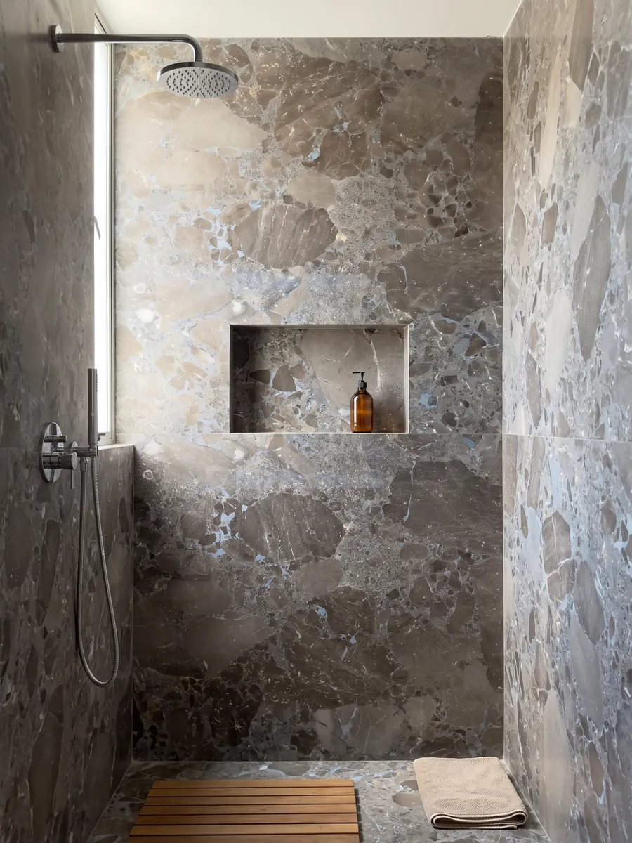 Shower clad in full gray Moon Grey marble slabs with a recessed niche: large angular fragments in grayish brown joined by a blue-gray matrix