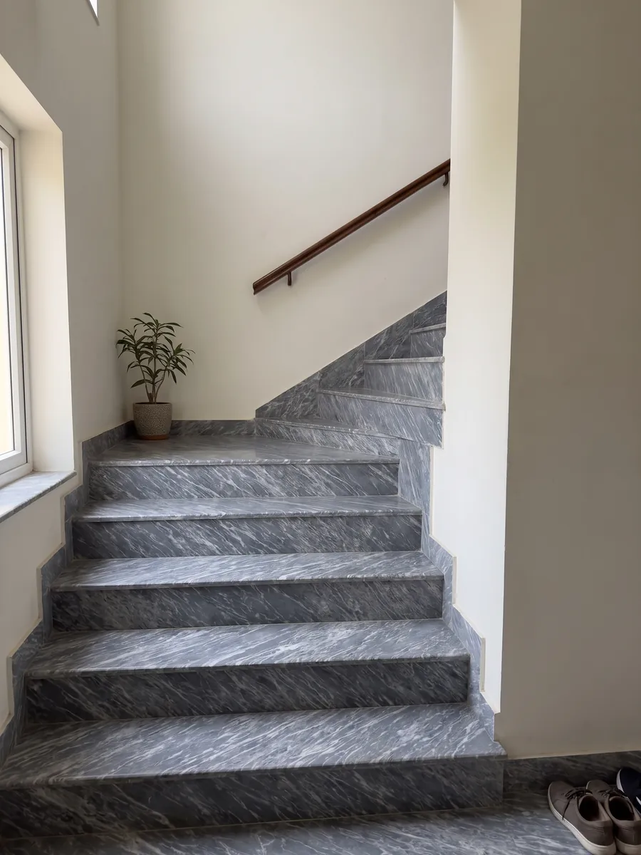 Interior staircase with Grigio Perla marble treads and a handrail: blue-gray covered in fine, parallel white streaks running diagonally