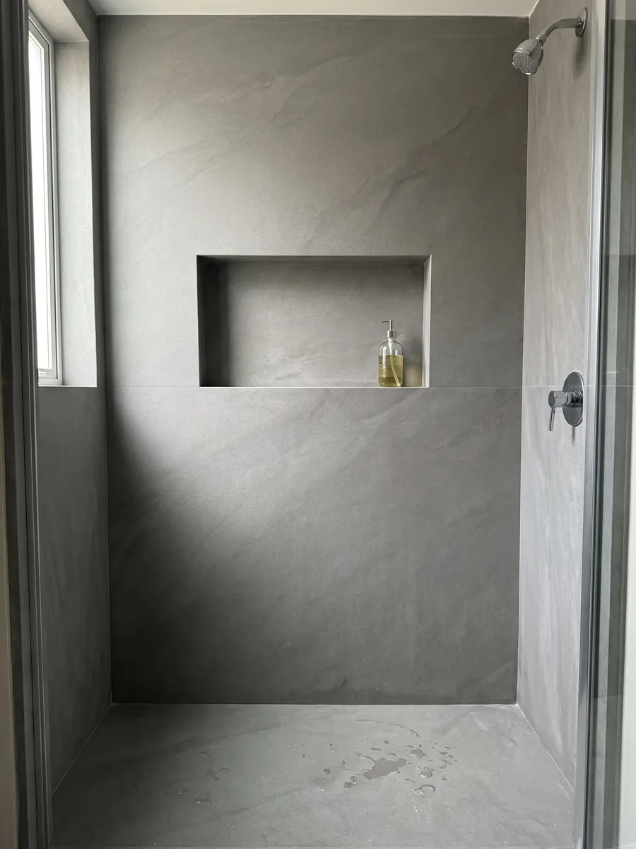 Shower clad in full gray Pietra Serena marble slabs with a recessed niche: smooth, even medium gray with no veins