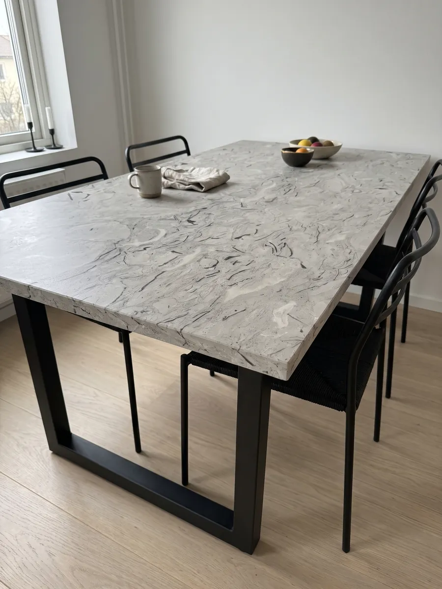 Dining table with a gray Repen marble top on a steel base: light gray with curved black fossil marks and horizontal clouds