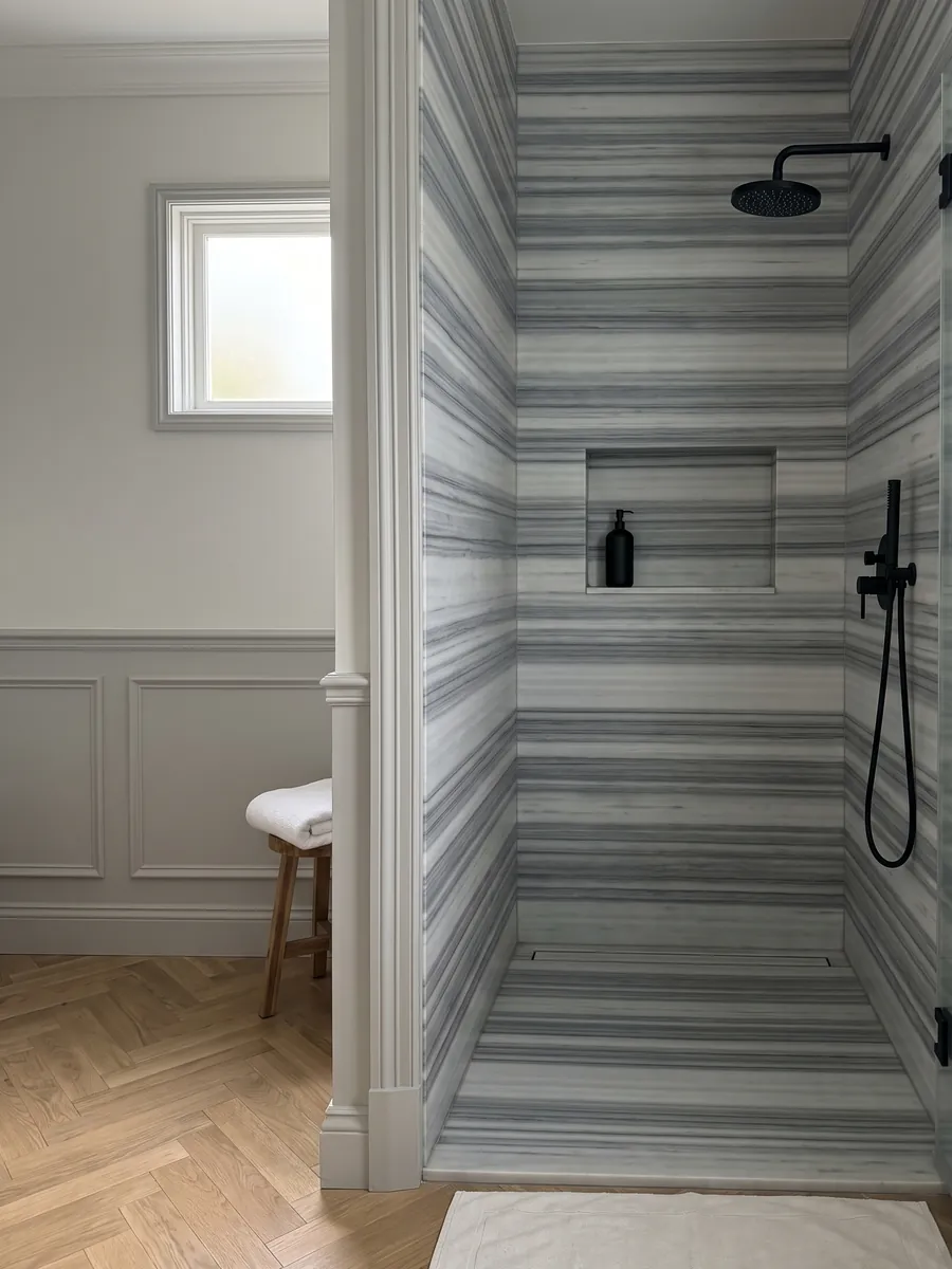 Shower clad in full slabs of gray Striato Olimpico marble with a recessed niche: perfectly parallel horizontal bands in blue-gray and white, like continuous stripes
