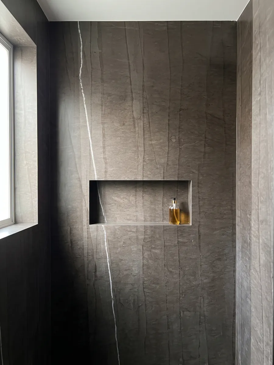 Shower clad in full slabs of Grigio Tao marble with a recessed niche: dark brown with faint vertical lines and a single fine white vein