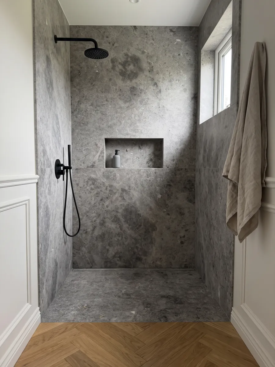 Shower clad in full slabs of Tundra gray marble with a recessed niche: medium gray with darker clouds and a fine speckling of light dots