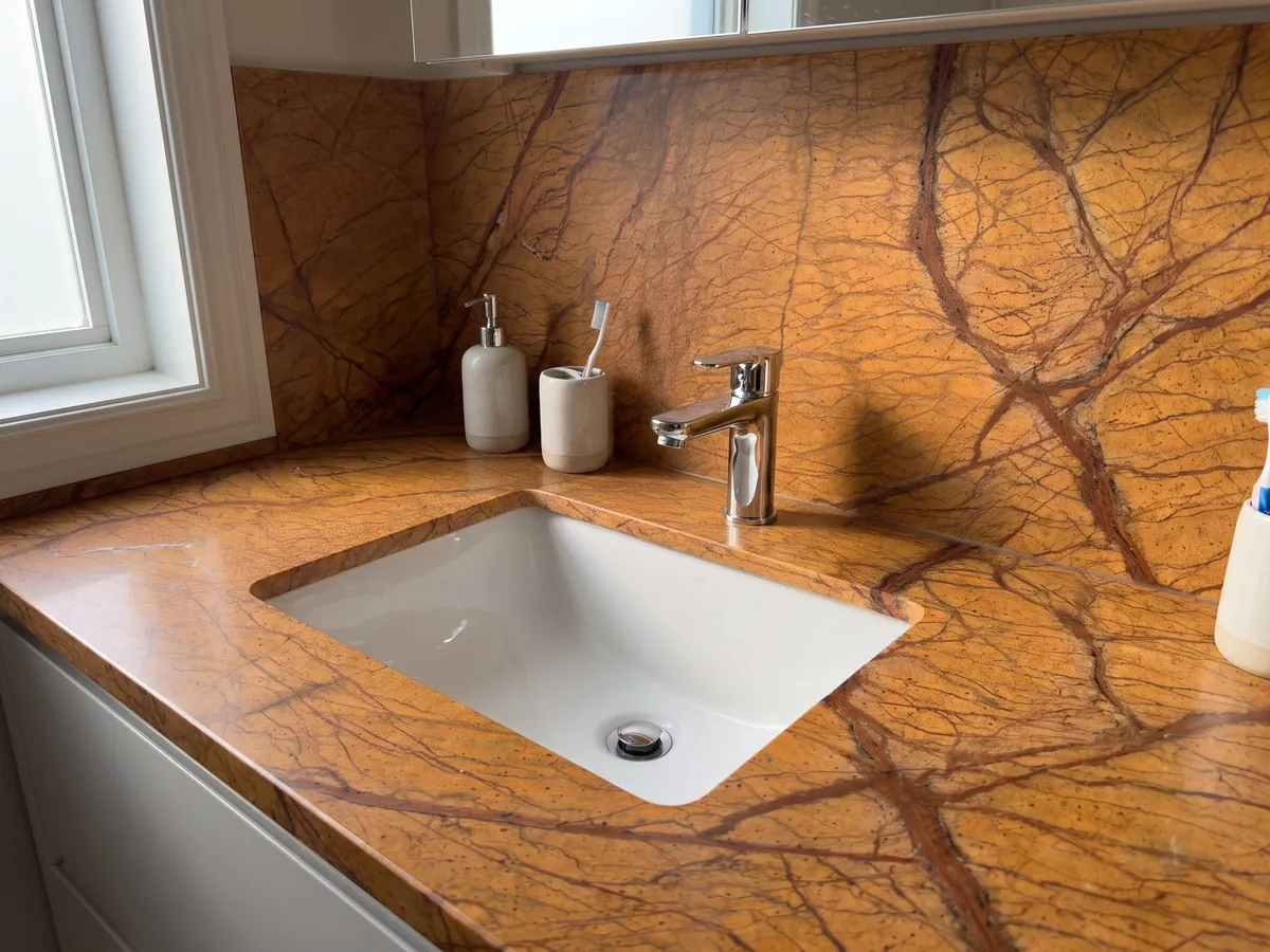 Vanity top and bathroom wall in Picasso Gold marble with a white sink and chrome fittings: intense ocher orange with a net of branching reddish brown veins
