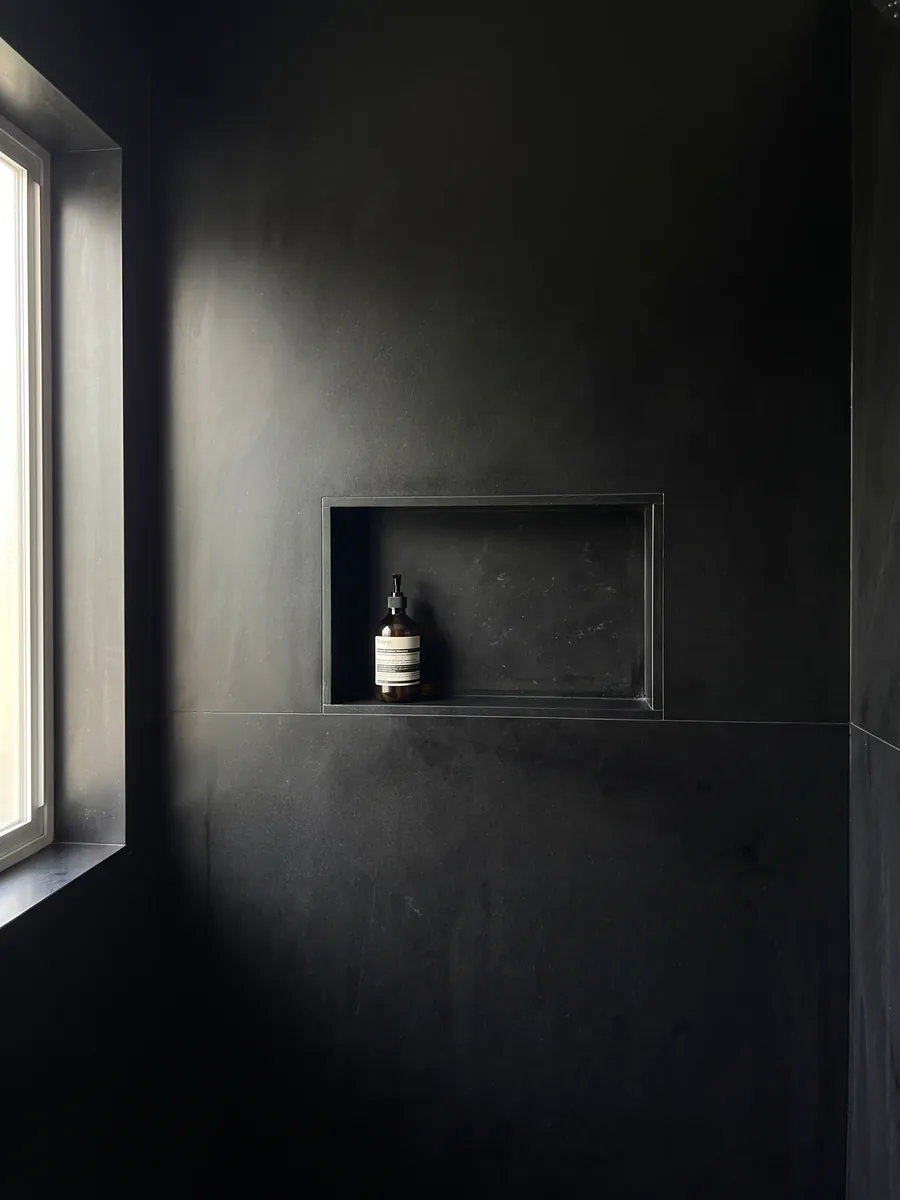 Shower clad in full slabs of Nero Belgio marble with a recessed niche: a completely plain, uniform black with no veins or marks