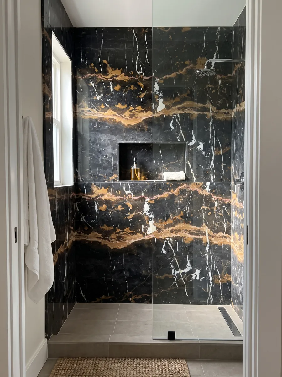 Shower clad in full slabs of Black & Gold black marble with a recessed niche: black with two horizontal golden ochre bands and vertical white veins
