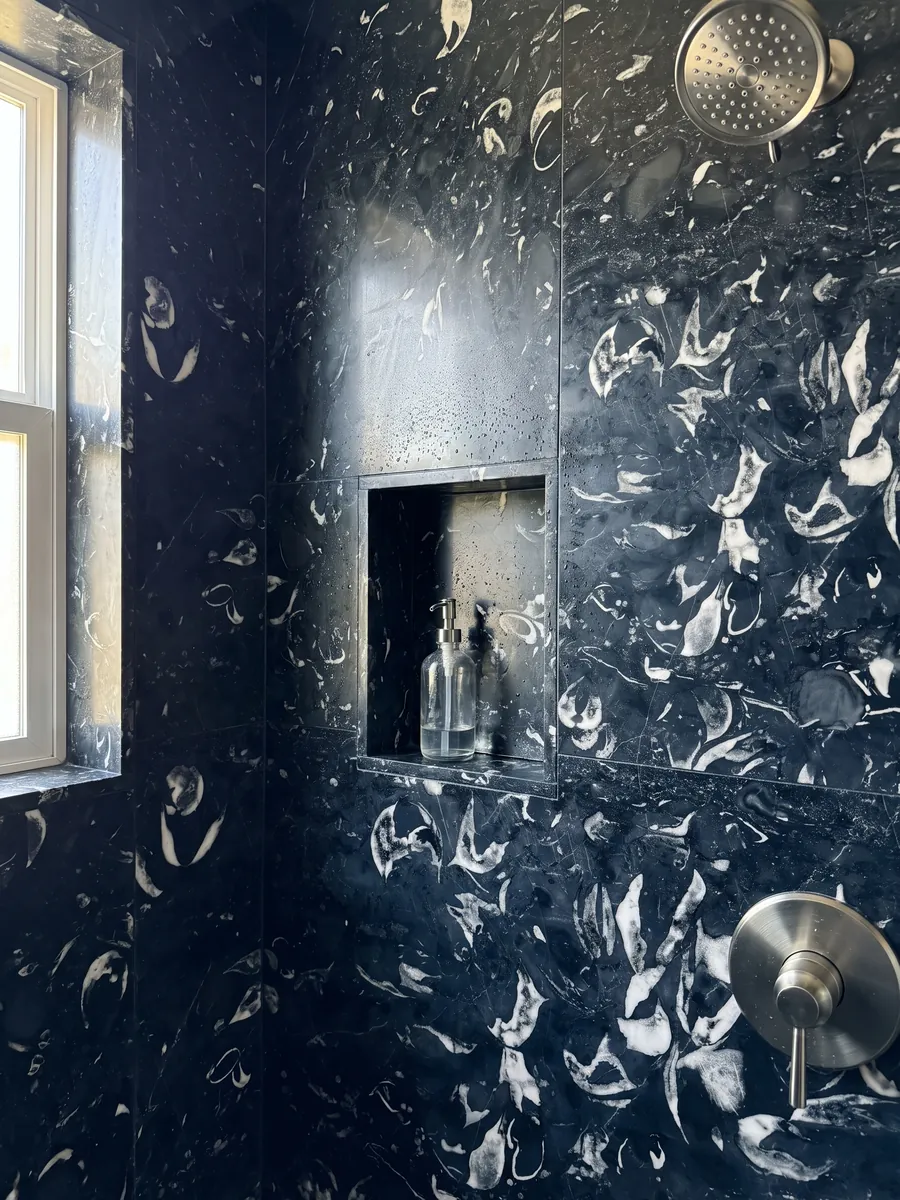 Shower clad in full Nero Boreale marble slabs with a recessed niche: blue-black with clearly visible curved white fossil shells