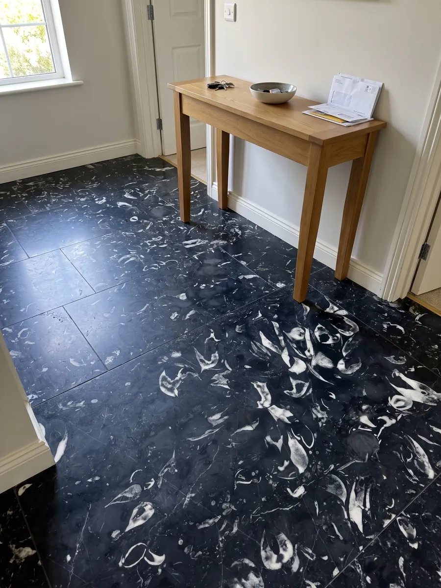 Entryway floor in large Nero Boreale marble slabs with natural light: blue-black with clearly visible curved white fossil shells