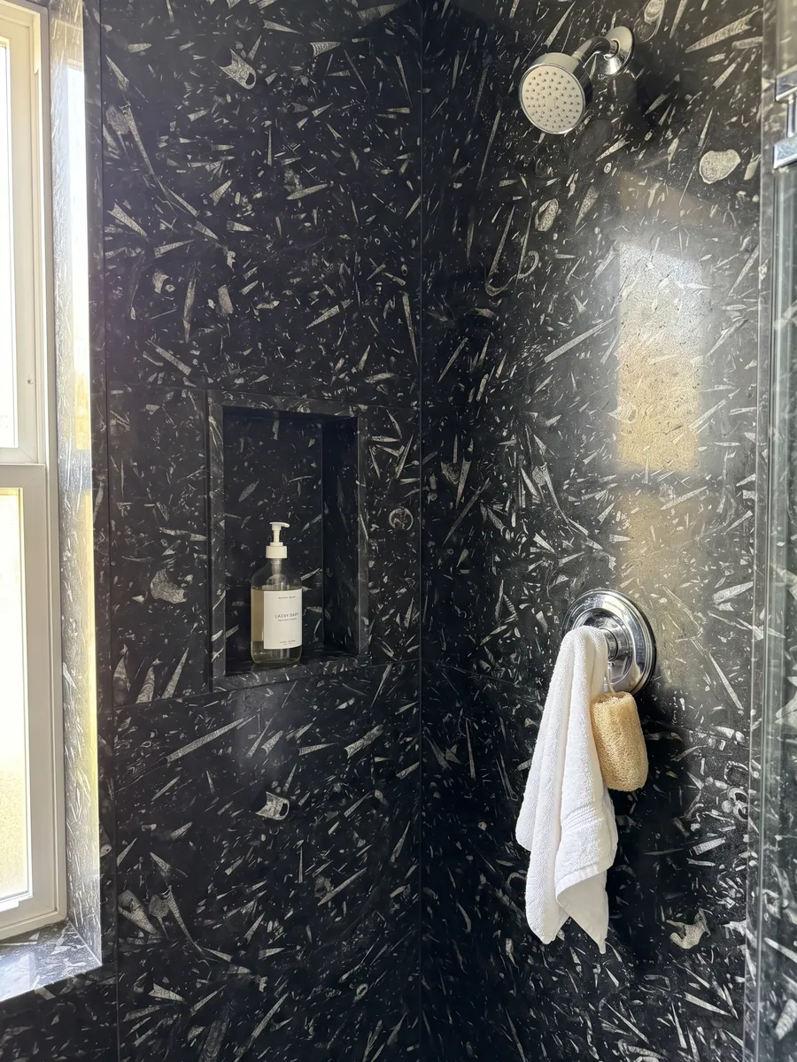 Shower clad in full slabs of black Fossil Black marble with a recessed niche: a black background full of elongated cone-shaped fossils in light gray