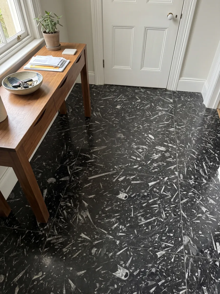 Entryway floor in large slabs of black Fossil Black marble with natural light: a black background full of elongated cone-shaped fossils in light gray